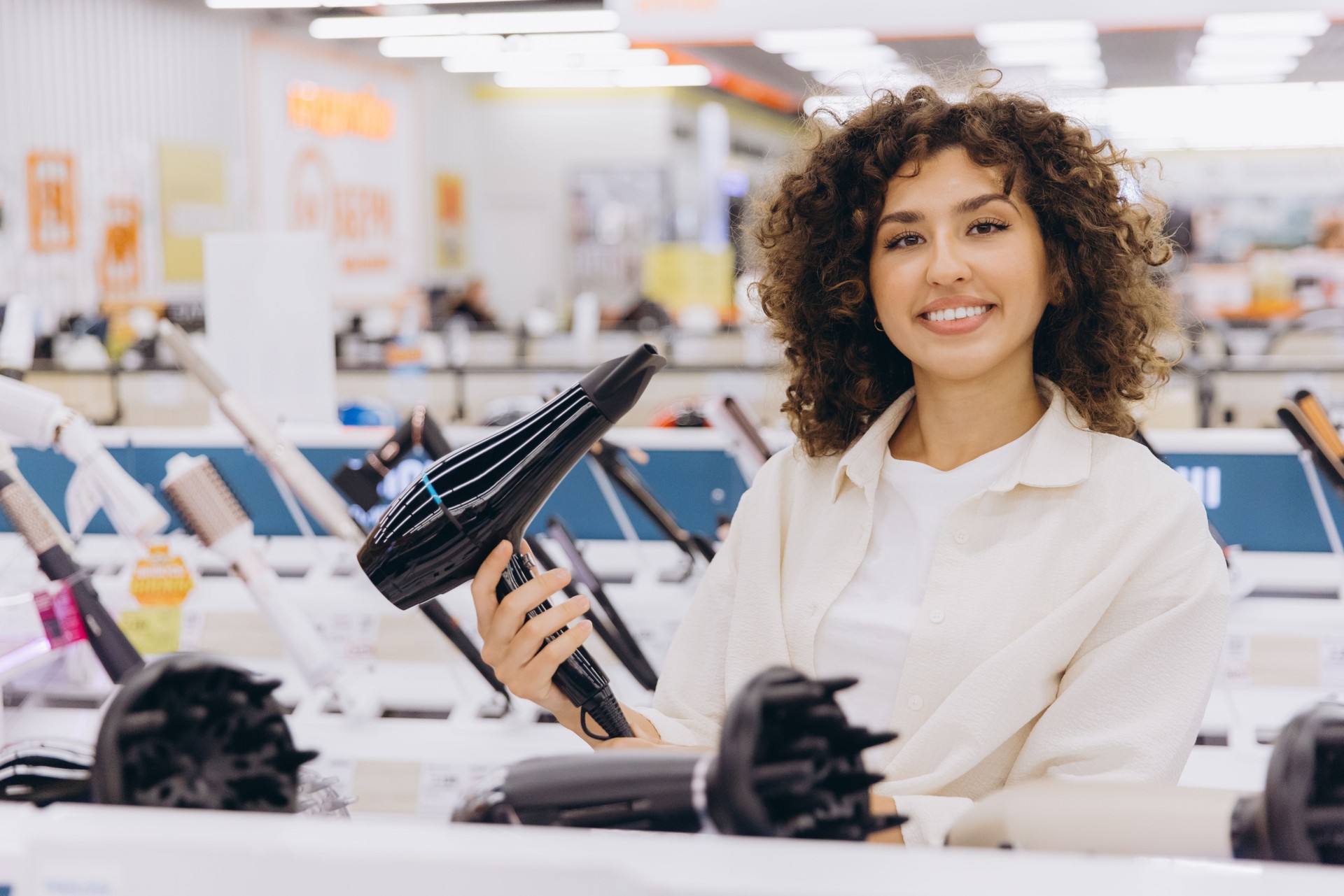 Woman choosing hairdryer in electronics store smiling and looking satisfied
